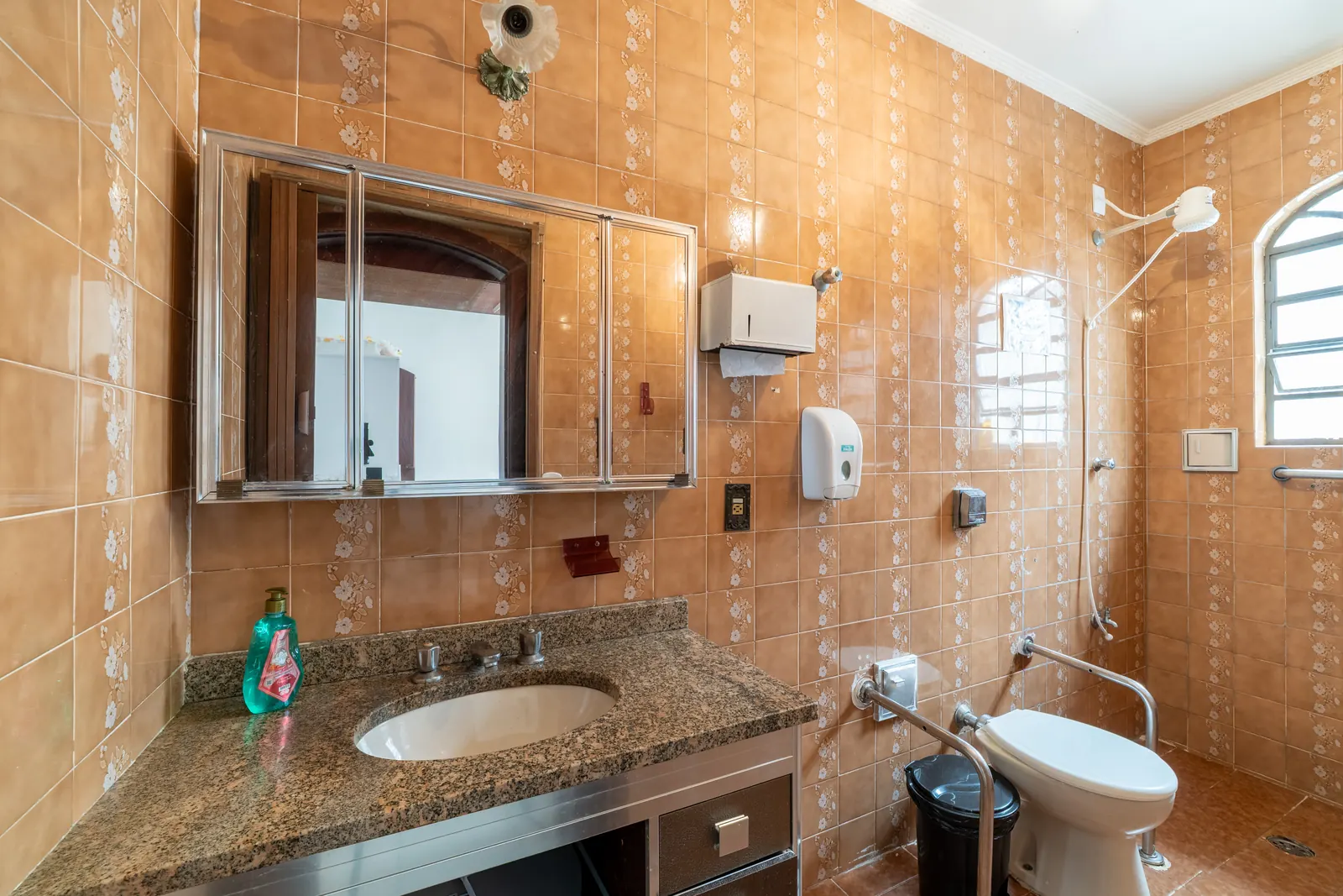 Banheiro com barras de apoio ao lado do vaso elevado, chuveiro e pia com armário