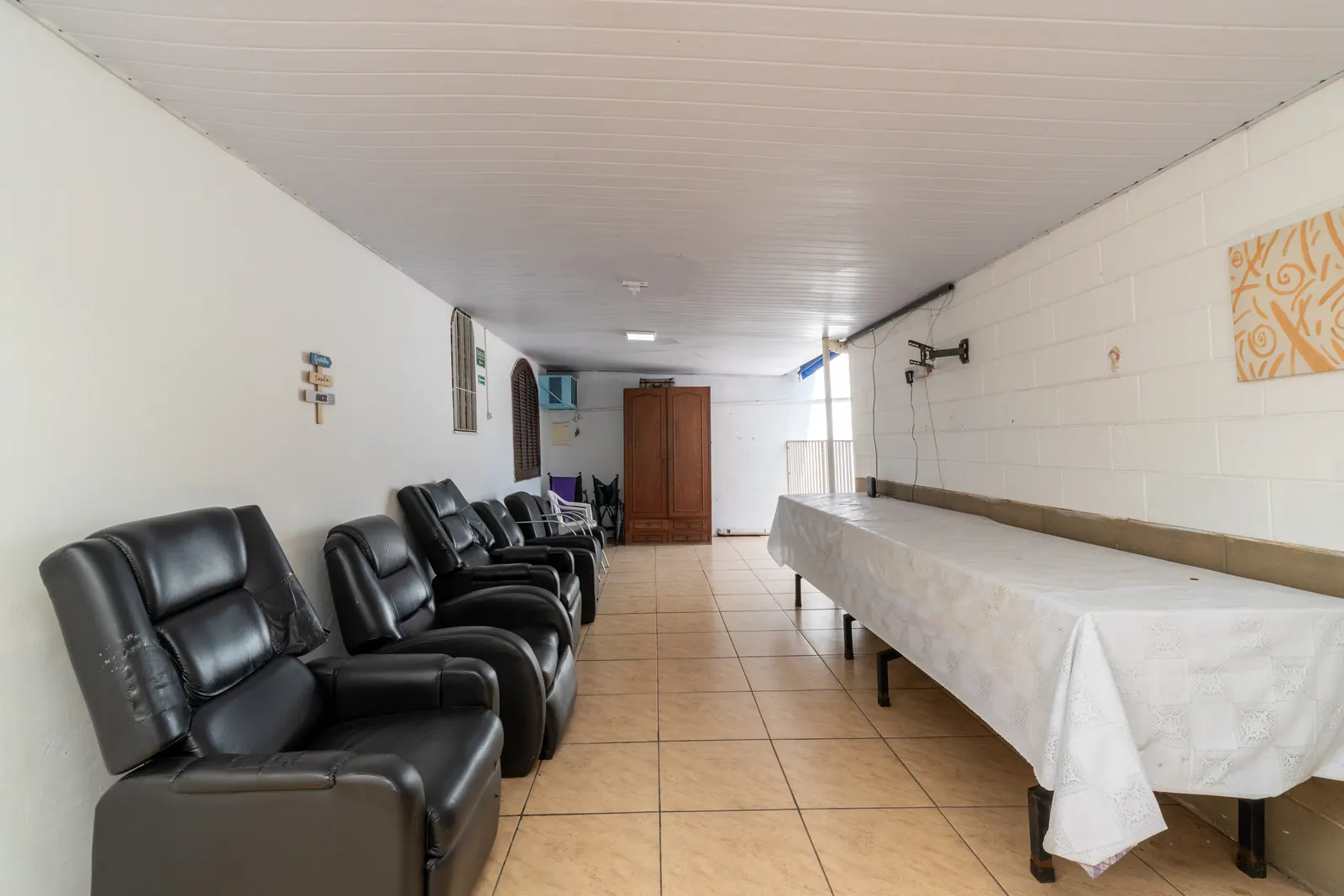 Sala comprida com poltronas reclináveis de um lado e uma mesa longa com toalha branca do outro
